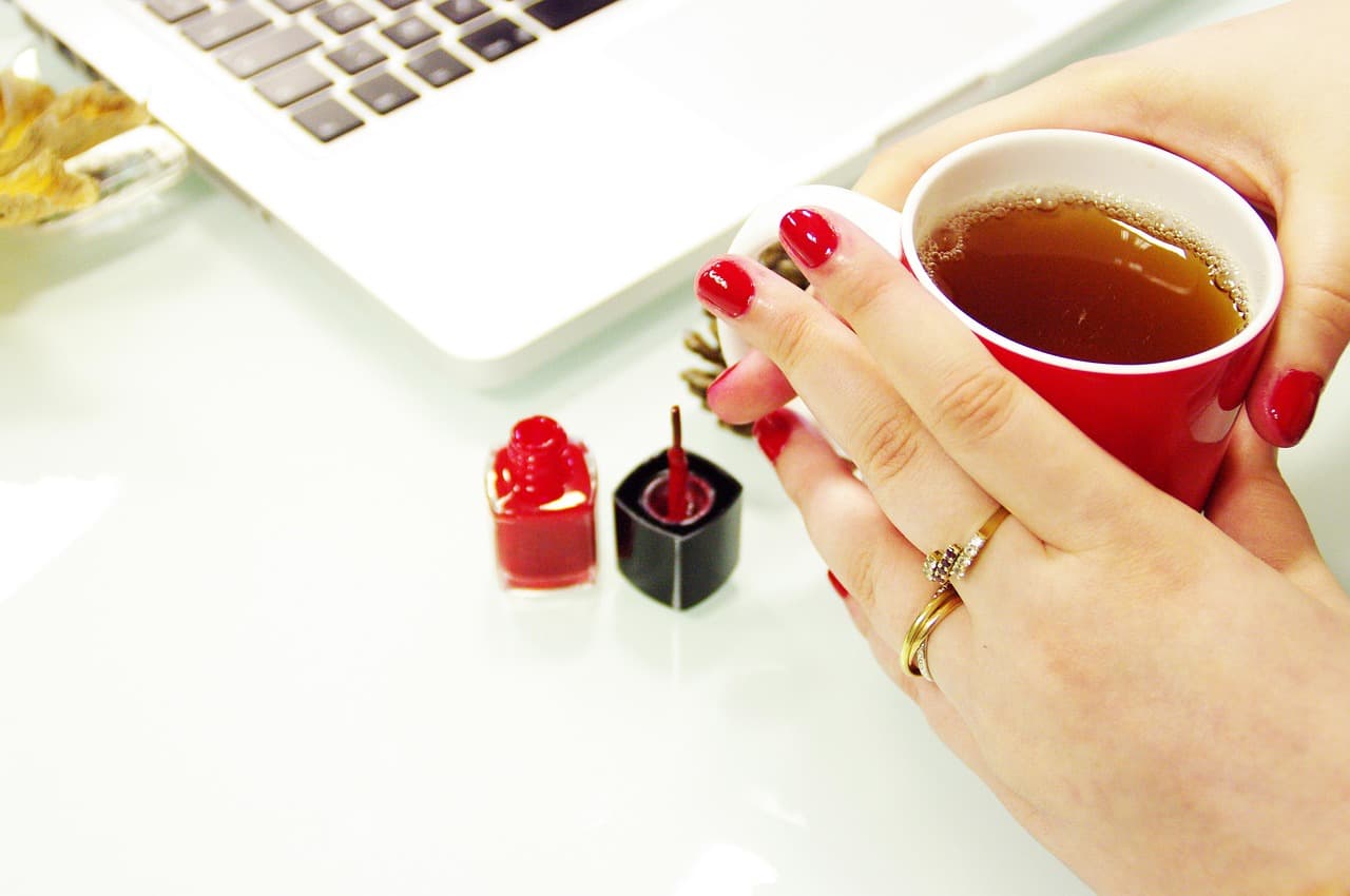 Red manicure holding a cup of tea beside nail polish